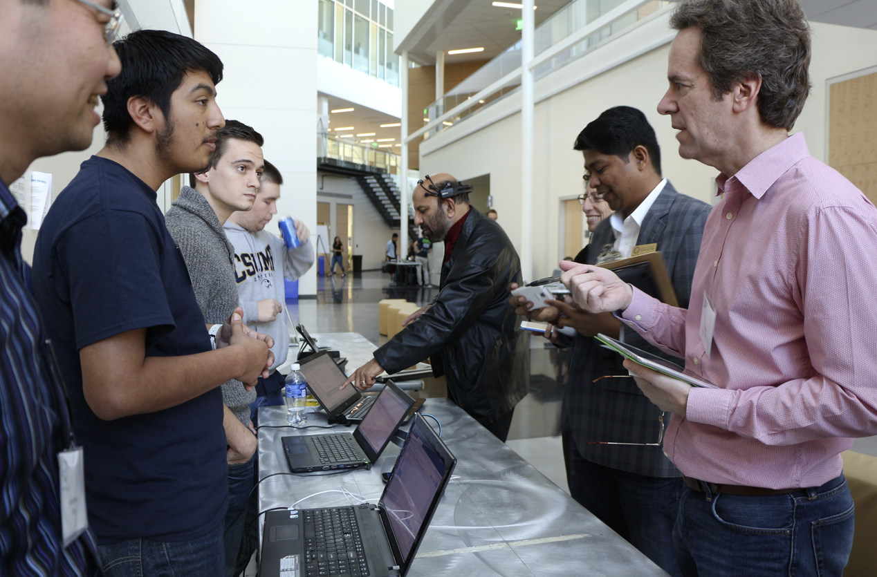 During the judging, Hackathon students Uriel Antonio and Andre Borner answered a technical question from Professor Glenn Bruns as Dean Shyam Kamath (in headset) tested the app, with Professor Sumadhur Shakya and Dean Marsha Moroh looking on. (Credit: Jan Janes Media)